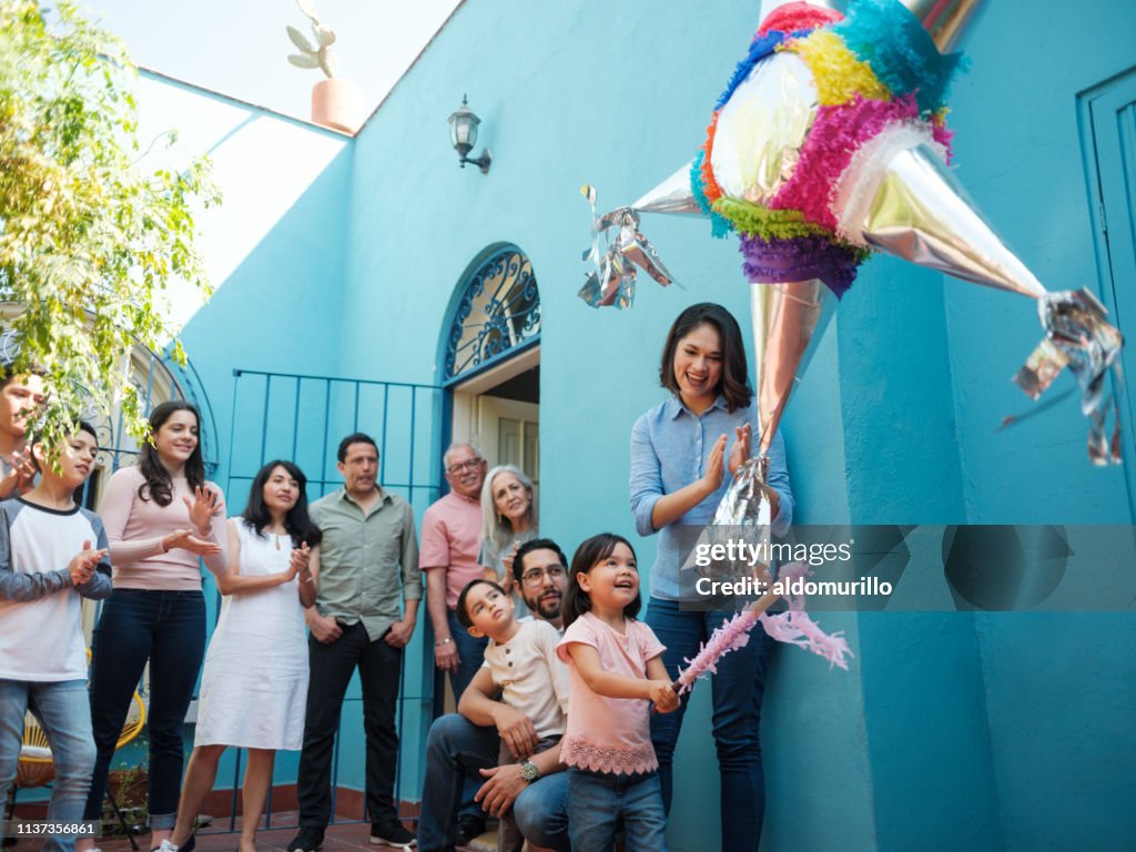 Feliz chica mexicana golpeando piñata con palo y familia buscando