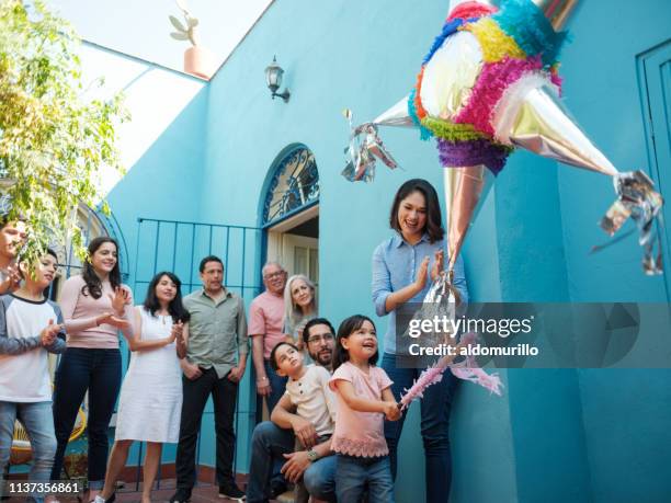 happy mexican girl hitting piñata with stick and family looking - piñata mexicana imagens e fotografias de stock