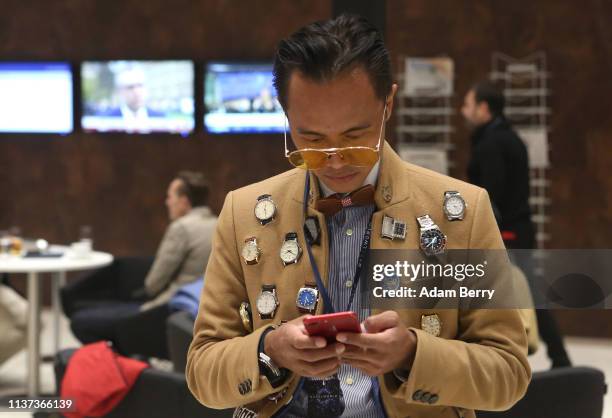 Visitor wearing a jacket covered in watches uses his mobile phone on the opening day of the 2019 Baselworld luxury watch and jewelry fair on March...