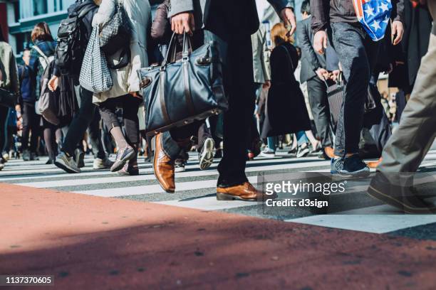 low section view of a crowd of busy commuters crossing street in shibuya crossroad, tokyo - hauptverkehrszeit stock-fotos und bilder