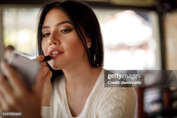 jonge vrouw toepassing lippenstift in een cafe - applying makeup stockfoto's en -beelden