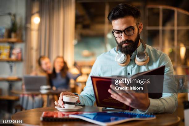 männliche studentin, die kaffee trinkt und ein buch liest. - male student wearing glasses with friends stock-fotos und bilder