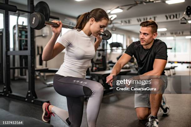 instructor de fitness guiando a la mujer joven cuando ella ejerce - instructor-de-acondicionamiento-físico fotografías e imágenes de stock