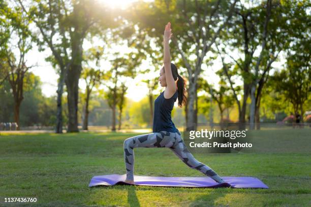 young asian woman practicing warrior 1 yoga in park at sunset. - yoga outdoor foto e immagini stock