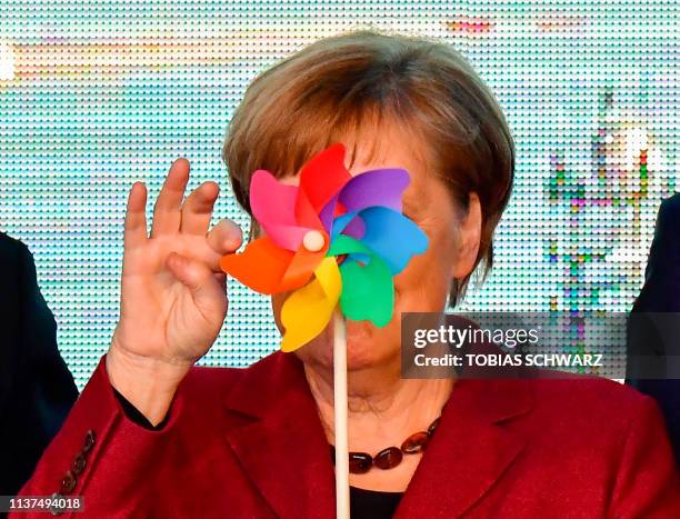 German Chancellor Angela Merkel is partly hidden by a toy wind wheel as she poses with children during the opening ceremony of the Arkona wind park...