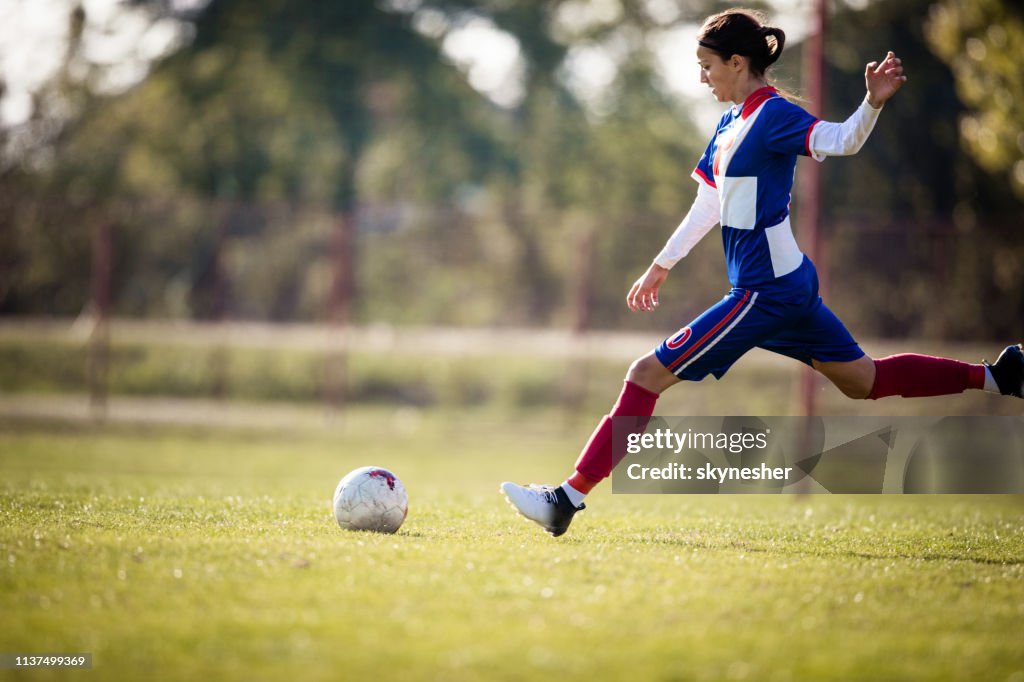 Teenage girl about to kick soccer ball on a playing field.