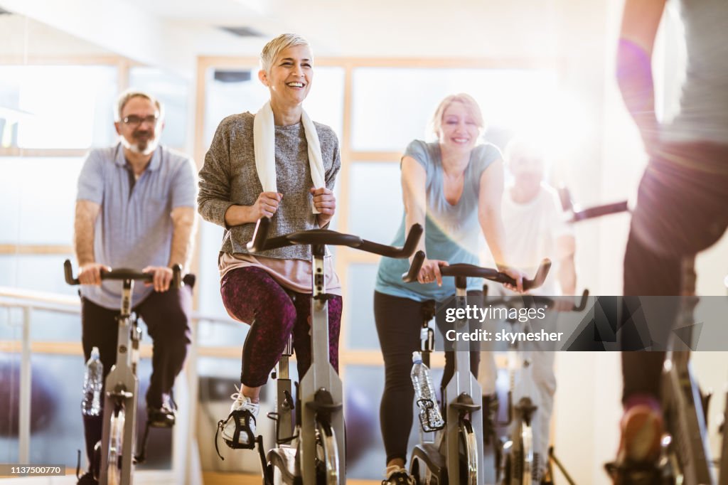 Gruppe von aktiven Senioren, die mit einem Instruktor in einem Fitnessstudio Spinnunterricht haben.