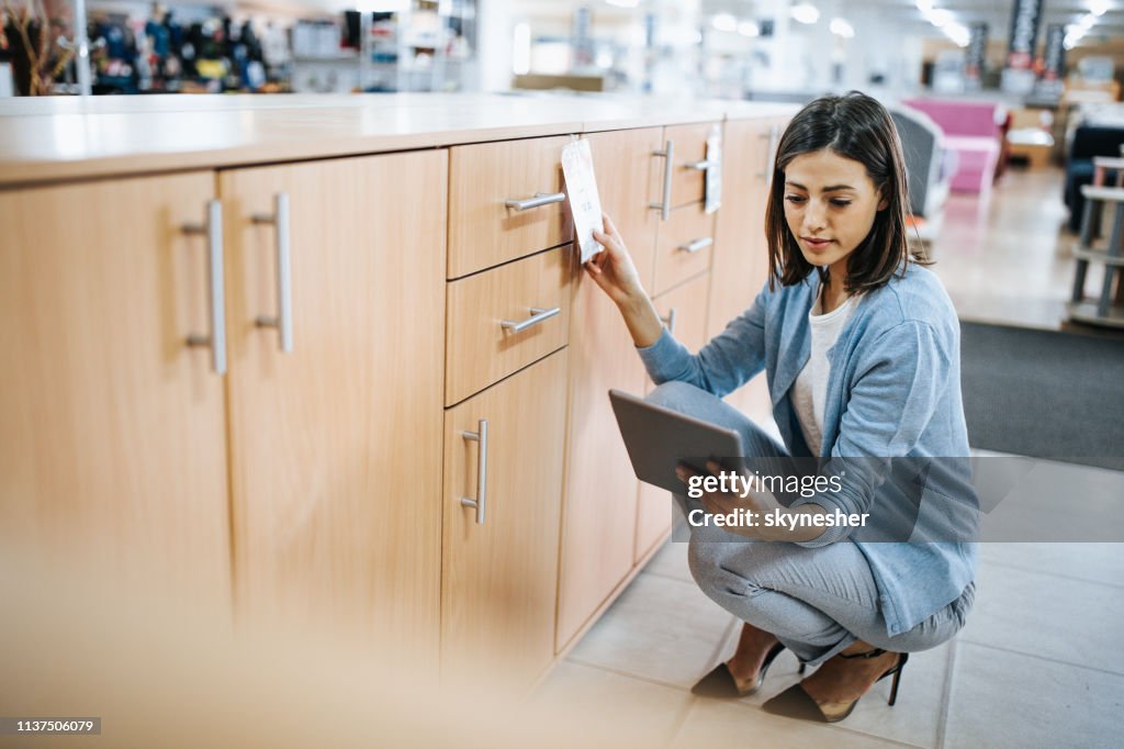 Junge Frau überprüft Preisschild, während Sie digitales Tablet im Möbelhaus.
