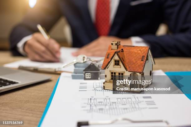 businessman signs contract behind home architectural model - mortgage financing stock-fotos und bilder