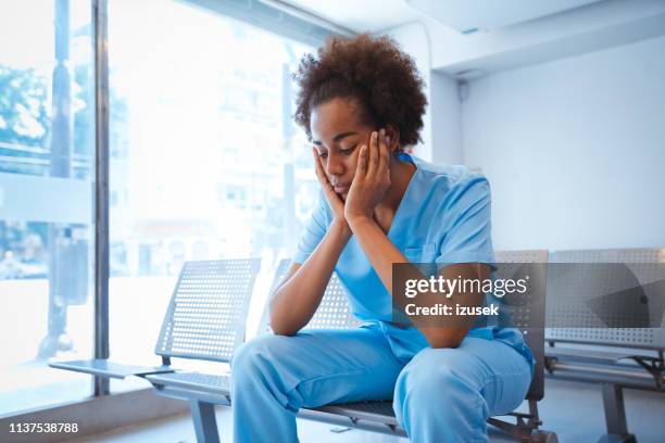 sad young female nurse sitting with hands on chin - sad nurse stock pictures, royalty-free photos & images