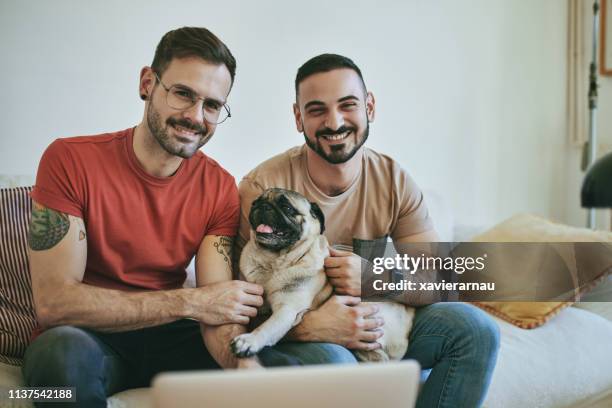 smiling homosexual couple with pug on sofa at home - pug portrait stock pictures, royalty-free photos & images