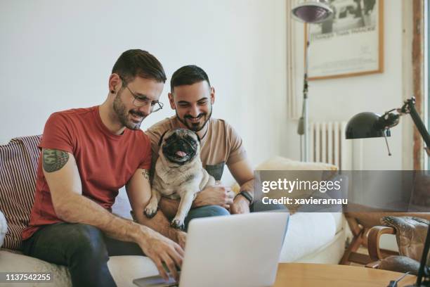 smiling gay couple with pug using laptop at home - casal gay imagens e fotografias de stock
