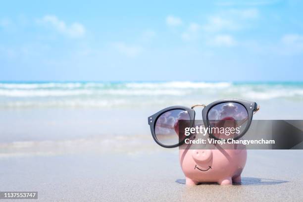 saving money for travel concept, pink piggy bank wearing sunglass on the beach - bank holiday fotografías e imágenes de stock