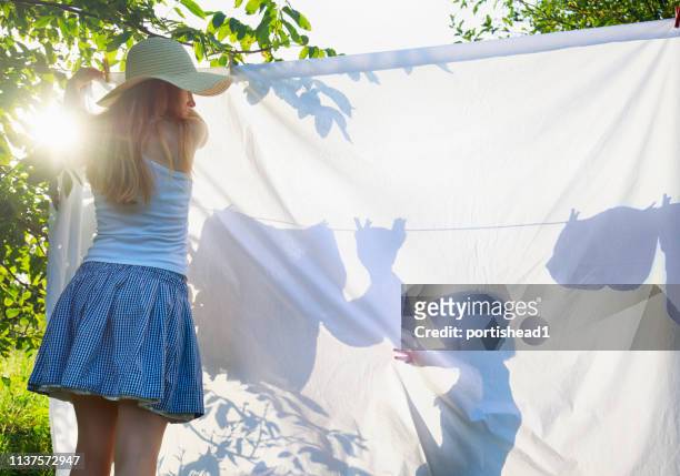 moeder en haar zoon opknoping wasgoed op een waslijn - bedsheets stockfoto's en -beelden
