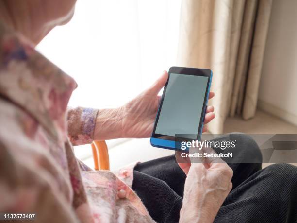 grandmother looking on cell phone at home - rear view hand window stock pictures, royalty-free photos & images