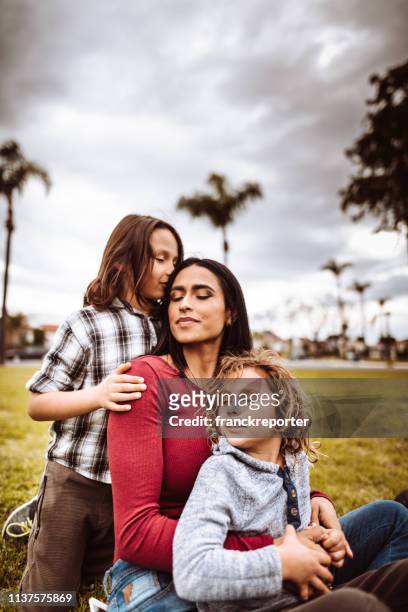 mother embrace the sons in a public park - tiny mexican girl stock pictures, royalty-free photos & images