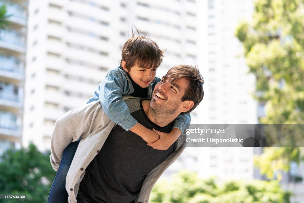 Handsome dad carrying son on back while both looking at each other smiling
