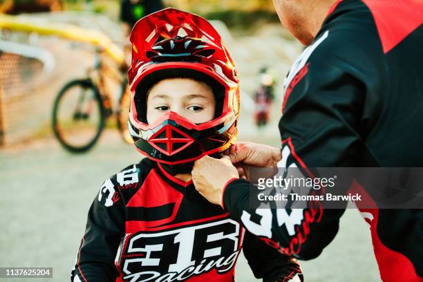 Father helping son buckle up helmet before BMX race