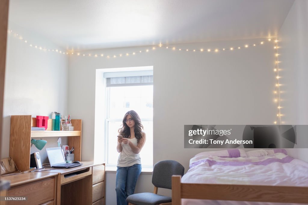Young woman college student in her dorm room with phone