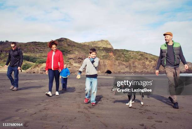 family and friends walking dog at beach in winter - new zealand family stock pictures, royalty-free photos & images