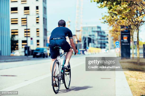 rear view of man riding racing bike on bicycle lane in the city - danish sports stock pictures, royalty-free photos & images