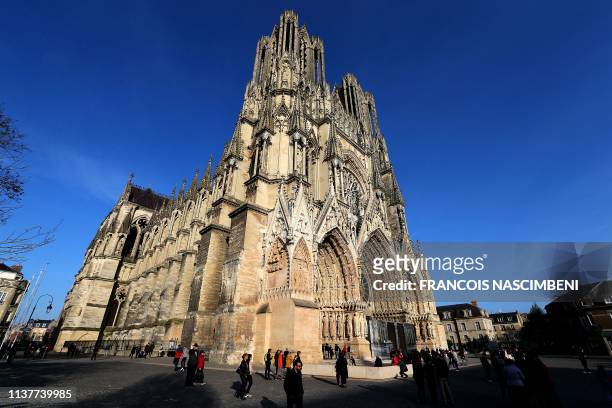People stand outside the Reims cathedral as the bells ring at 1650 GMT to mark the exact moment when the fire started at the Notre-Dame de Paris...