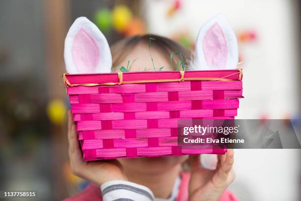 child (6-7) hiding face behind pink easter basket and rabbit ears - easter basket - fotografias e filmes do acervo