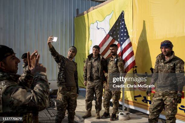 Syrian Democratic Forces fighters pose for a photo with the American flag on stage after a SDF victory ceremony announcing the defeat of ISIL in...