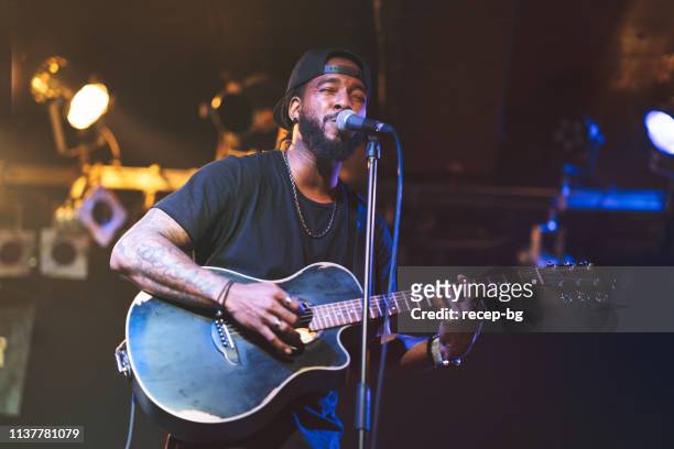black man playing acoustic guitar and singing on stage - rock musician stock pictures, royalty-free photos & images