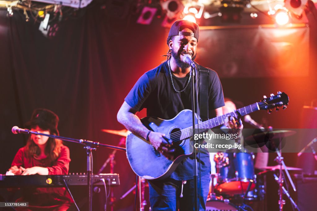 Black male guitarist singing and playing acoustic guitar on stage