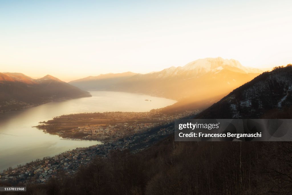 Sunlight illuminates the Lake Maggiore and villages of Ascona and Locarno. Canton of Ticino, Switzerland, Europe.