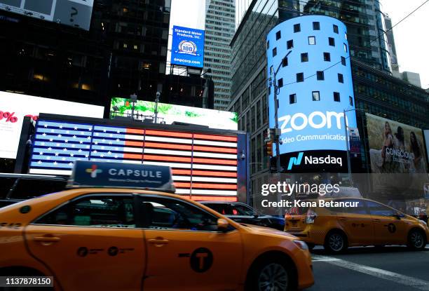 People pass walk by the Nasdaq building as the screen shows the logo of the video-conferencing software company Zoom after the opening bell ceremony...