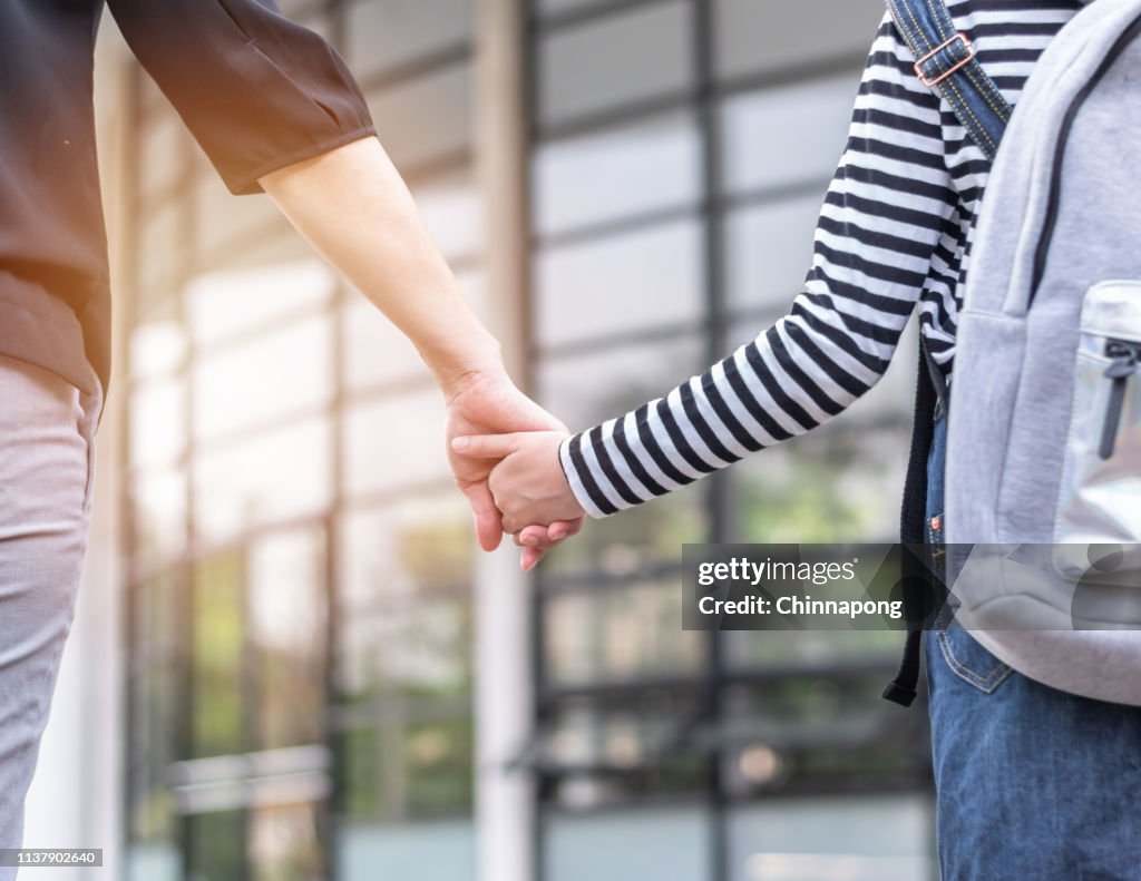 Educational back to school, parent's day, bring kid to work concept with elementary student girl carrying backpack holding woman or mother's hand walking up admission office building going to class