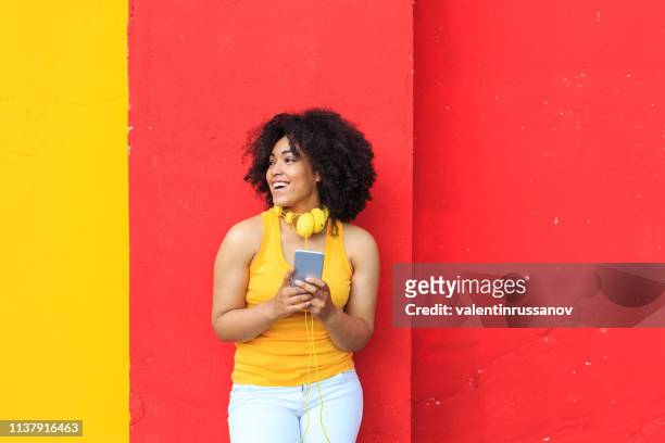 femme de sourire écoutant la musique et utilisant le téléphone intelligent - portrait femme fond rouge adulte photos et images de collection
