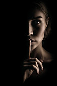 The girl shows a sign of silence. Face on black background, close-up