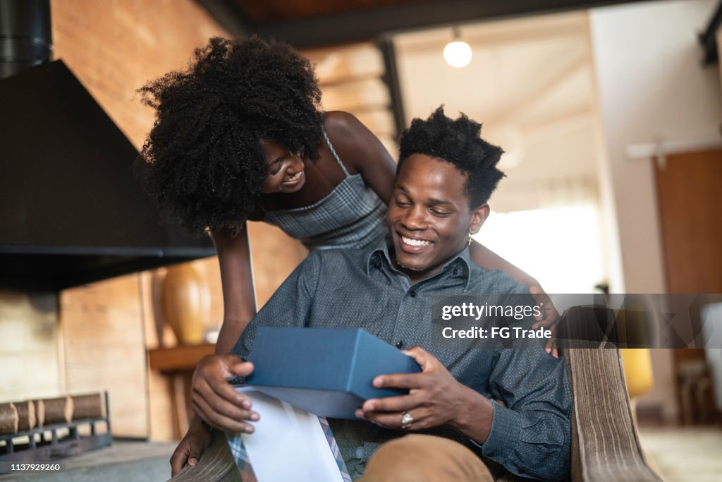 Wife making a surprise giving a present to her husband at home