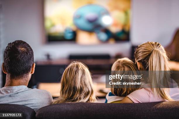 rear view of a family watching tv on sofa at home. - family watching tv from behind stock pictures, royalty-free photos & images