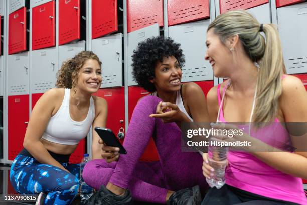 diverse freundinnen entspannen sich nach dem training im fitnessstudio und im umkleideraum im gespräch und lächeln - umkleideraum stock-fotos und bilder