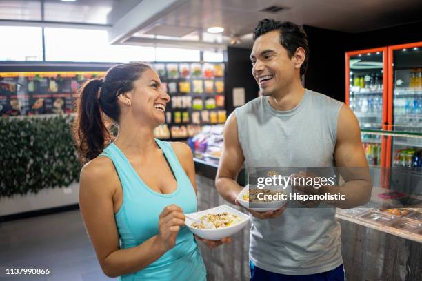 cheerful young couple at the gym enjoying a bowl of cereal after working out laughing - flirting gym stock pictures, royalty-free photos & images