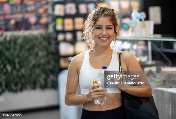 portret van mooie jonge vrouw na het trainen in de sportschool met een waterfles en graanreep - cereal bar stockfoto's en -beelden