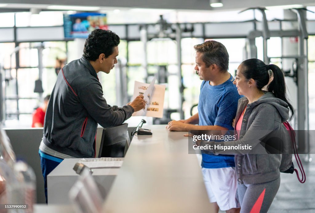 Happy couple registering at the gym while employee explains benefits showing them a catalogue