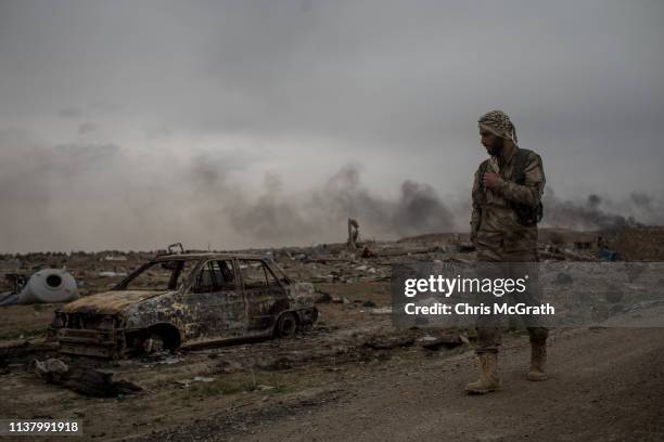 Syrian Democratic Forces fighter walks past destroyed vehicles in the final ISIL encampment on March 24, 2019 in Baghouz, Syria. The Kurdish-led and...