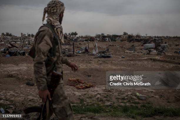 Syrian Democratic Forces fighter walks past destroyed vehicles in the final ISIL encampment on March 24, 2019 in Baghouz, Syria. The Kurdish-led and...