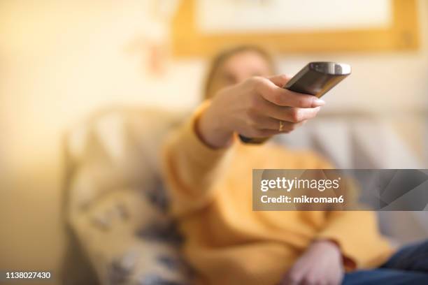 cropped hand of woman operating remote at home - turning on or off stockfoto's en -beelden