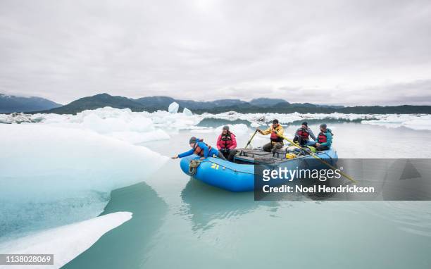 Young boy leaning out of raft to touch iceberg