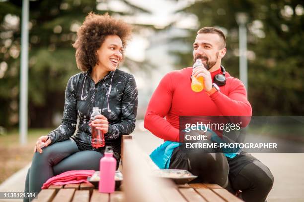 jonge atletische paar hydraterende zelf tijdens het nemen van een pauze na het sporten in een stadspark - monster energy stockfoto's en -beelden