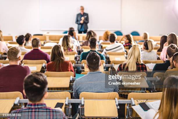 rear view of large group of students on a class at lecture hall. - adult student stock pictures, royalty-free photos & images