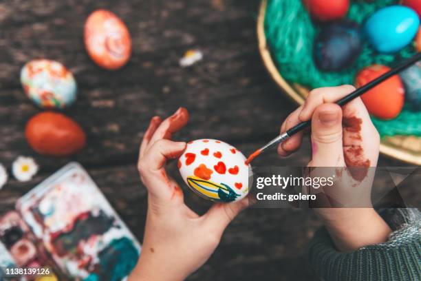 niña pequeña pintando huevo de pascua en la vieja mesa de madera - easter family fotografías e imágenes de stock