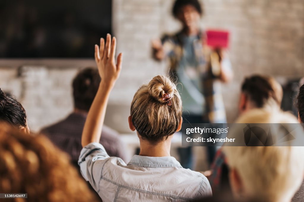 Rückenbild einer Frau will eine Frage zu einem Seminar stellen.