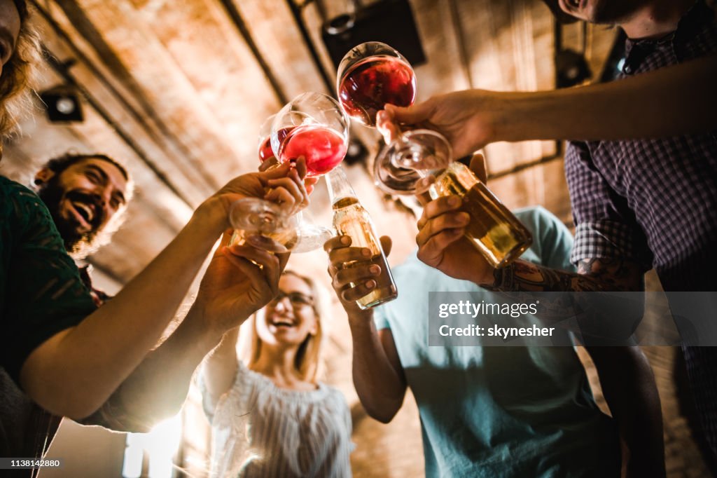 Below view of happy friends toasting with alcohol on a party.